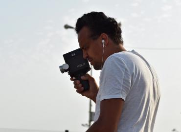 Side view of Justin Randolph Thompson holding a Super 8 camera to his face as he films